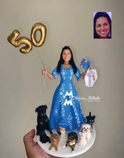 Boneca de biscuit de mulher com vestido azul florido, balões dourados 50, sacola de compras e cachorros e gatos aos pés
