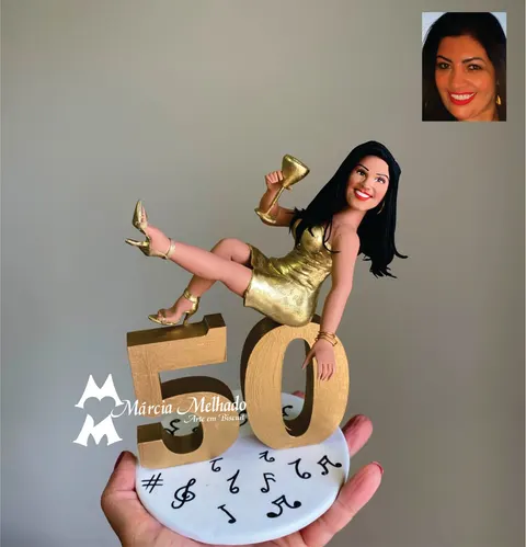 Boneca de biscuit de vestido dourado sentada sobre o número 50 dourado erguendo uma taça, em base com notas musicais