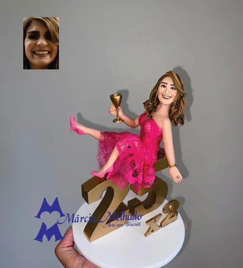 Boneca de biscuit de mulher com vestido pink de renda sentada sobre o número 25 dourado, com x2 ao lado e taça na mão