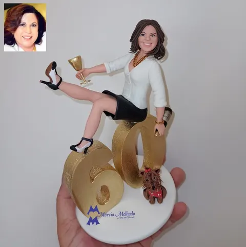 Boneca de biscuit de mulher sentada sobre o número 60 dourado erguendo uma taça, com espumante e cachorro yorkshire