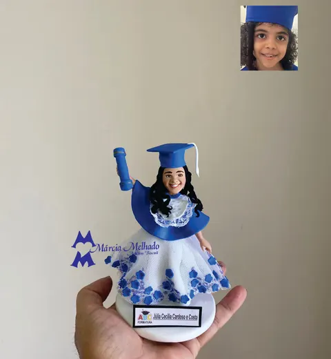 Boneca de biscuit de menina sorridente com capelo e beca azuis, canudo erguido e vestido branco de tule com flores azuis