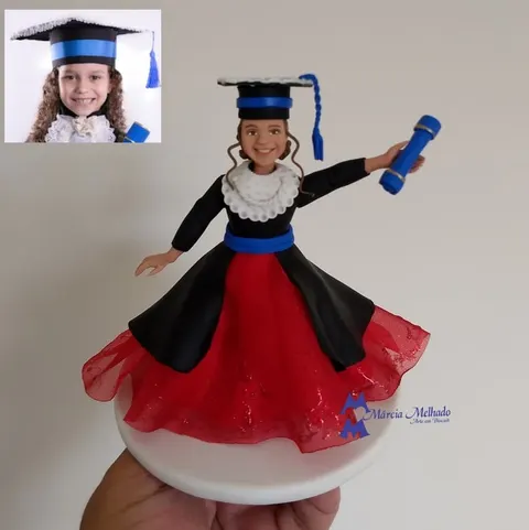 Boneca de biscuit de menina formanda com beca preta, saia de tule vermelha, capelo com fita azul e canudo de diploma