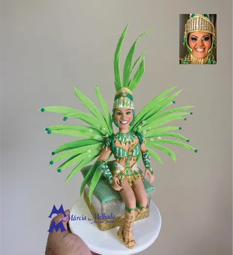 Boneca de biscuit vestida de passista de escola de samba, com capacete e plumas verdes, sentada em caixa dourada