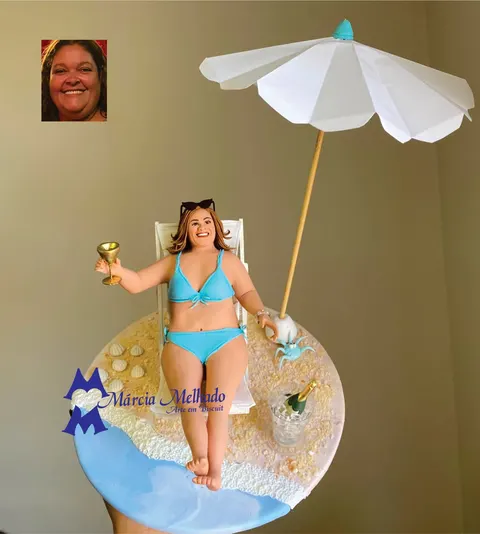 Boneca de biscuit de biquíni azul deitada em espreguiçadeira na areia, com taça, guarda-sol branco e balde de champanhe