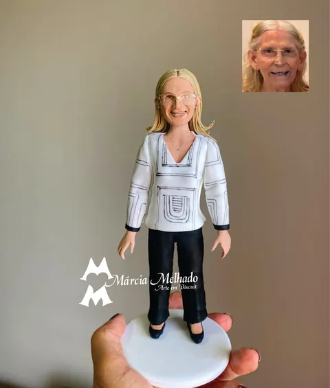 Boneca de biscuit de senhora loira com óculos, blusa branca com bordados pretos e calça preta, sobre base branca
