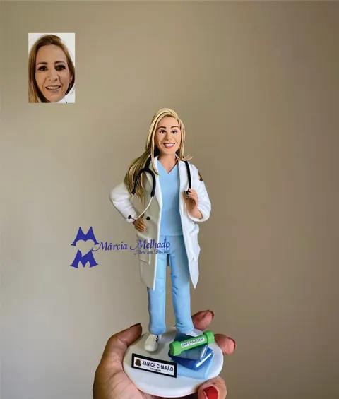 Boneca de biscuit de enfermeira loira com jaleco branco, pijama azul e estetoscópio, com livros e canudo na base