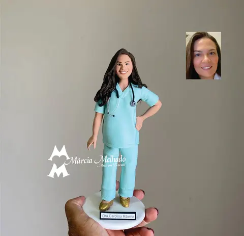 Boneca de biscuit de médica de cabelos castanhos com pijama cirúrgico azul claro, estetoscópio no pescoço e mão na cintura