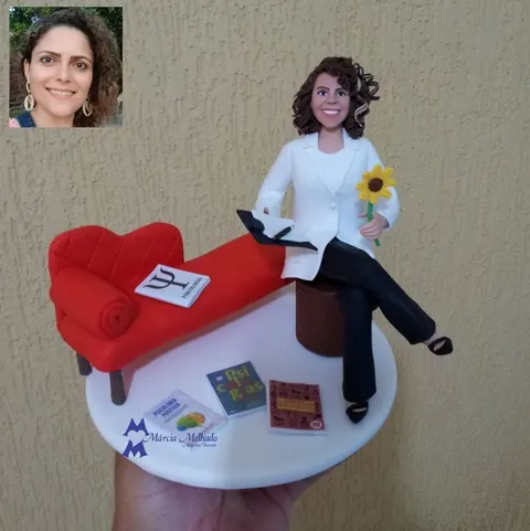 Boneca de biscuit de psicóloga sentada com prancheta e girassol, ao lado de um divã vermelho e livros de psicologia