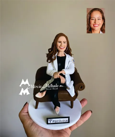 Boneca de biscuit de psicóloga ruiva de jaleco branco sentada de pernas cruzadas numa poltrona marrom