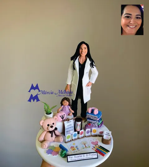 Boneca de biscuit psicóloga de jaleco branco em pé entre ursinho, boneca, cérebro com símbolo psi, cartas de emoções e livros