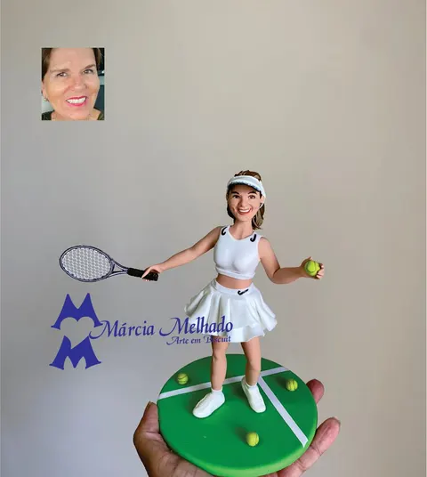 Boneca de biscuit de tenista com viseira, roupa branca e raquete, em pé sobre base verde de quadra de tênis com bolinhas