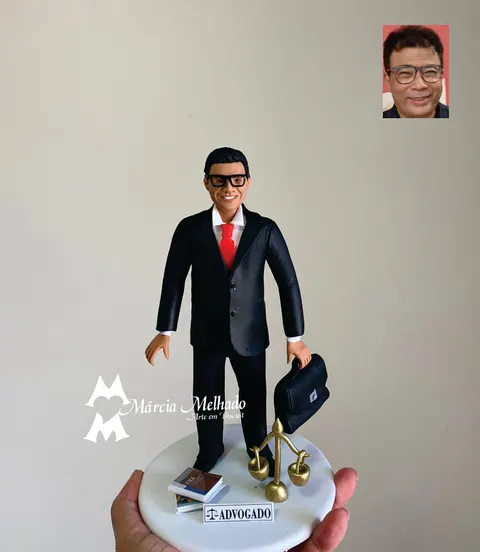 Boneco de biscuit de advogado de terno preto e gravata vermelha segurando maleta, com balança dourada e livros na base