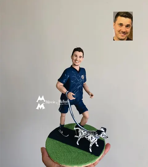 Boneco de biscuit de homem correndo com camiseta azul-marinho e bermuda, segurando a coleira de um cachorro dálmata