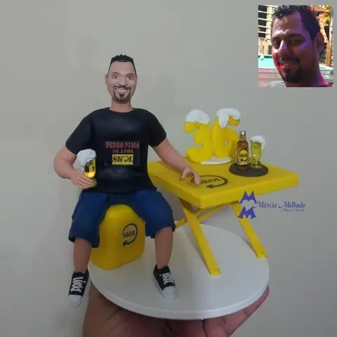 Boneco de camiseta preta sentado em engradado amarelo de cerveja com copo de chope e mesa de bar com número 36