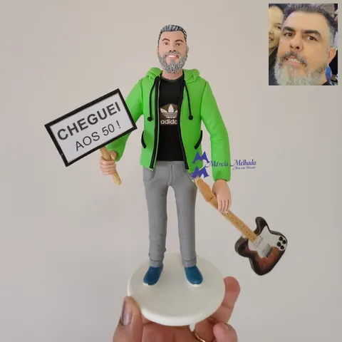 Boneco de biscuit de homem grisalho com moletom verde segurando plaquinha Cheguei aos 50 e guitarra elétrica