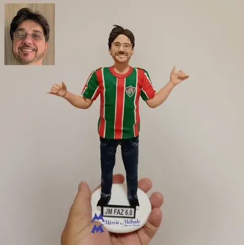 Boneco de óculos com camisa listrada do Fluminense e calça jeans, braços abertos, sobre base com plaquinha de 60 anos
