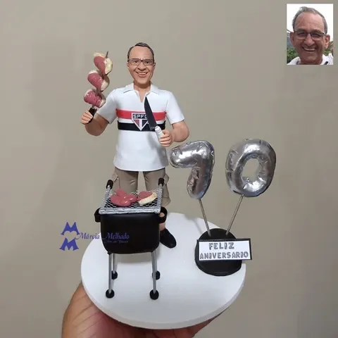 Boneco de óculos com camisa do São Paulo segurando espeto de carne e faca, churrasqueira e balões prateados do número 70