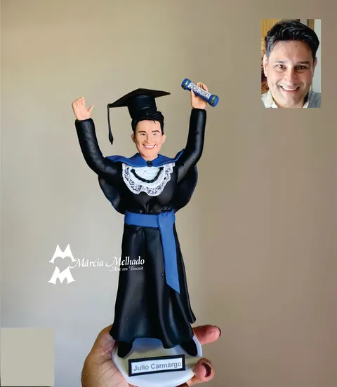 Boneco de biscuit de formando de beca preta com faixa azul, capelo e canudo de ciências contábeis erguido