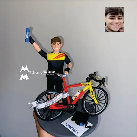 Boneco de biscuit de formando com camisa de ciclismo erguendo o canudo azul, ao lado de bicicleta speed vermelha e amarela