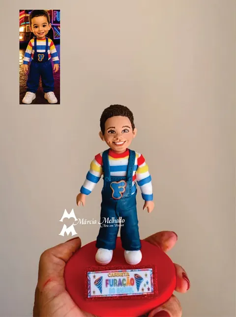 Boneco de biscuit de menino com blusa listrada colorida e macacão jeans com letra F, sobre base vermelha com plaquinha