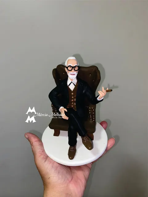Boneco de biscuit de senhor de barba branca e óculos redondos, de terno, sentado em poltrona marrom com charuto