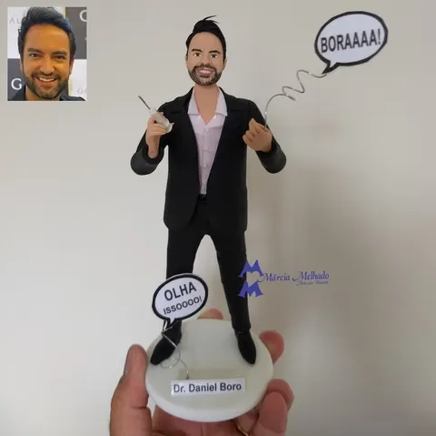 Boneco de biscuit de terno preto e camisa rosa segurando seringa, com dois balões de fala e plaquinha de doutor na base