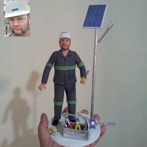 Boneco de biscuit de eletricista de uniforme cinza e capacete branco com alicate, ao lado de poste com painel solar