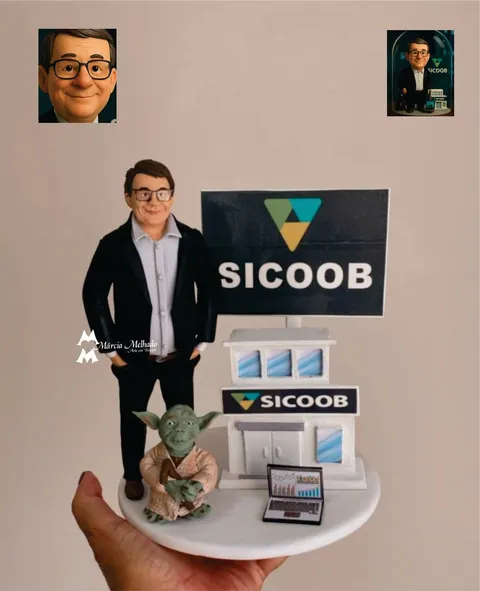 Boneco de biscuit de terno preto e óculos ao lado de uma agência do Sicoob em miniatura, com notebook e Yoda na base
