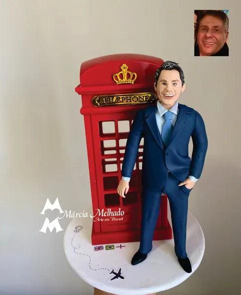 Boneco de biscuit de homem de terno azul-marinho ao lado de cabine telefônica vermelha de Londres com bandeiras na base