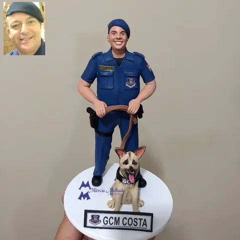 Boneco de biscuit de guarda civil municipal de farda azul e boina segurando a guia de um cão pastor com colete GCM