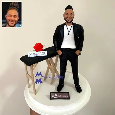 Boneco de biscuit de homem de barba com blazer preto ao lado de maca de massagem com rosas vermelhas e placa Permita-se