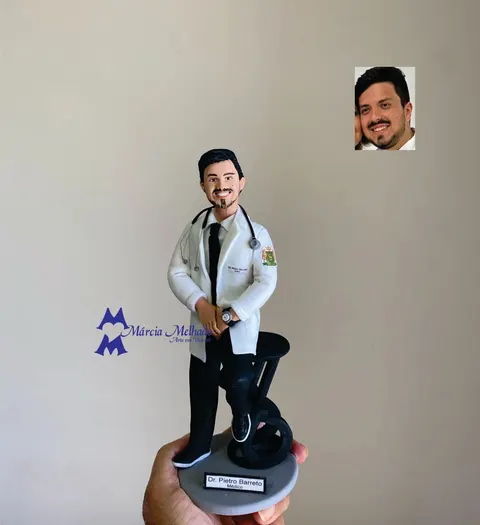 Boneco de biscuit médico de jaleco branco, gravata preta e estetoscópio no pescoço apoiado em banco alto preto