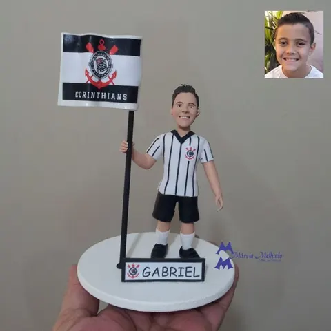 Boneco de biscuit de menino com camisa do Corinthians segurando bandeira do time sobre base branca