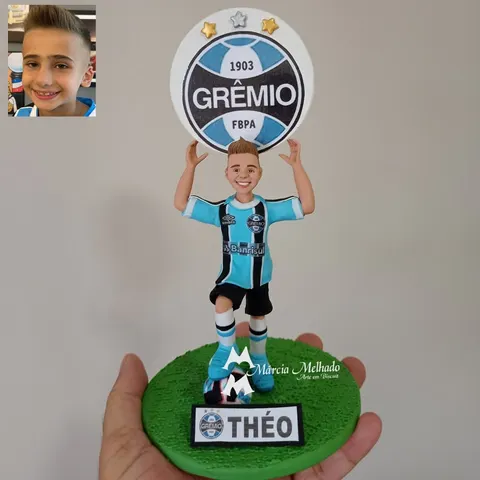 Boneco de biscuit de menino com camisa do Grêmio erguendo o escudo do time, bola no pé e base de grama