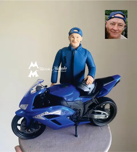Boneco de biscuit de homem de boné virado e jaqueta azul com a mão sobre o capacete em cima de uma moto esportiva azul Suzuki