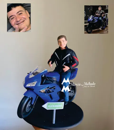 Boneco de biscuit de motociclista com jaqueta preta e vermelha sentado em moto esportiva azul, com placa de estrada na base