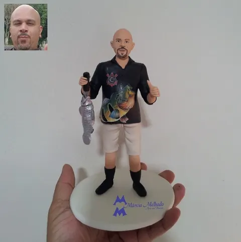 Boneco de biscuit de pescador careca com camisa preta do Corinthians, bermuda bege, segurando um peixe e fazendo joinha