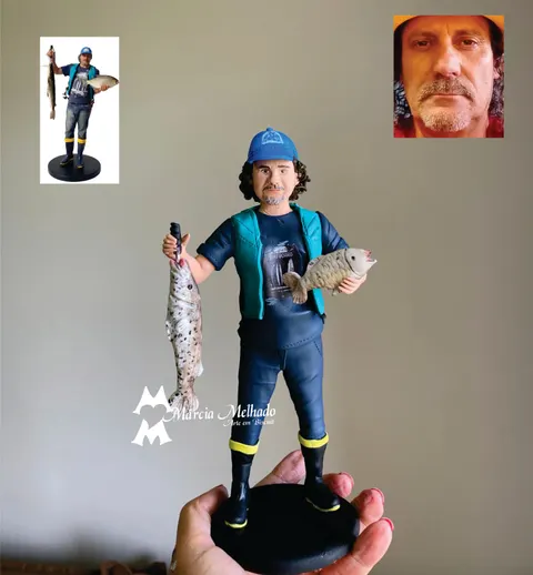 Boneco de biscuit de pescador com boné azul, colete verde-água, calça jeans e botas, segurando um peixe em cada mão