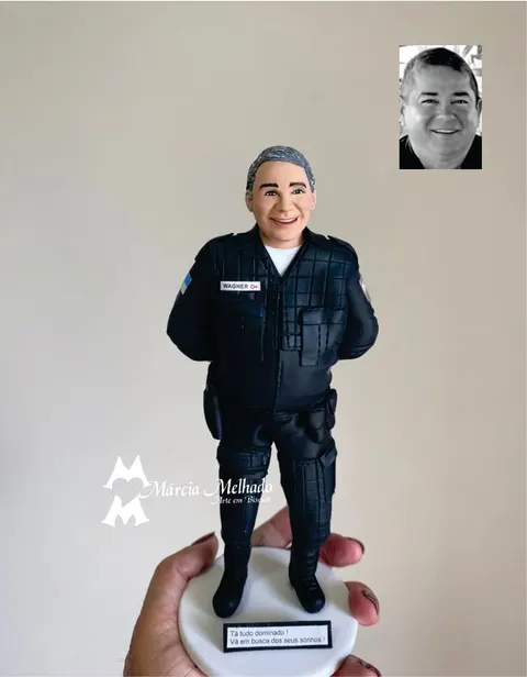 Boneco de biscuit de policial grisalho de farda tática preta, com as mãos atrás do corpo, sobre base branca com plaquinha