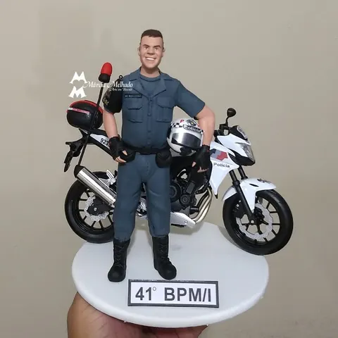 Boneco de biscuit de policial militar com capacete na mão ao lado de moto branca da polícia e plaquinha 41º BPM/I