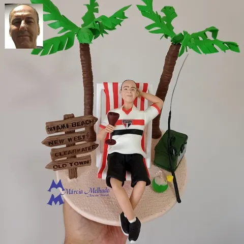 Boneco de biscuit com camisa do São Paulo relaxando em cadeira de praia entre coqueiros, com taça de vinho e vara de pesca