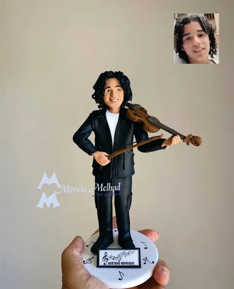 Boneco de biscuit de jovem de cabelo cacheado e terno preto tocando violino sobre base branca com notas musicais e plaquinha.