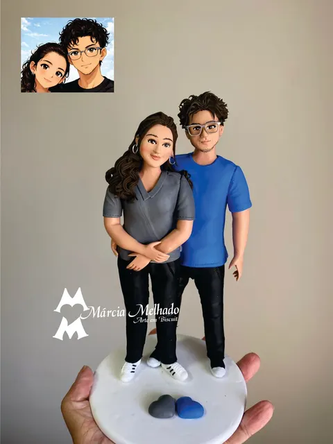 Bonecos de biscuit de casal abraçado, moça cacheada de blusa cinza e rapaz de óculos com camiseta azul, corações na base