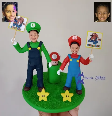 Topo de bolo de biscuit com dois meninos vestidos de Luigi e Mario segurando plaquinhas de aniversário sobre base de grama