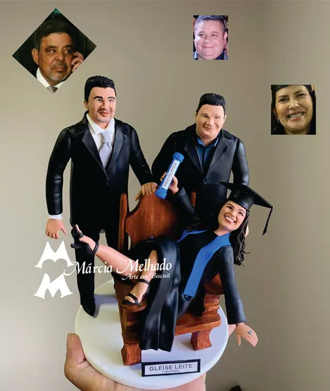 Bonecos de biscuit de formanda em psicologia com beca e capelo em cadeira de madeira entre dois homens de terno preto.