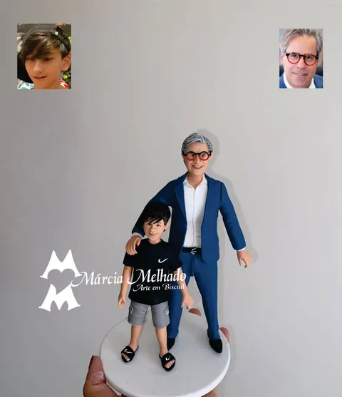 Boneco de biscuit de homem grisalho com óculos vermelhos e terno azul abraçando menino de boné e camiseta preta
