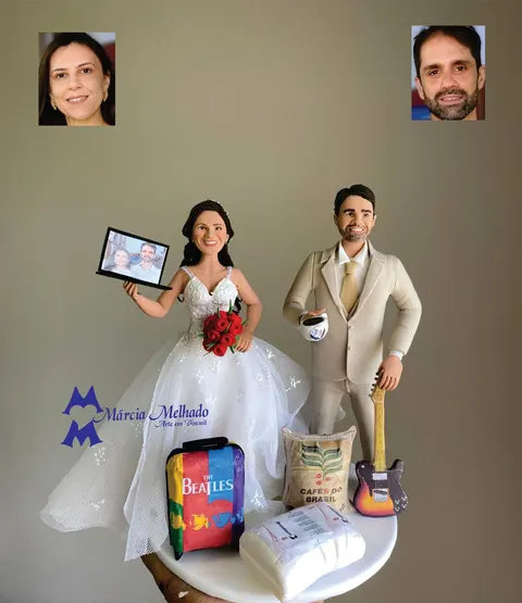 Noivinhos de biscuit: noiva com buquê de rosas e notebook, noivo de terno bege com guitarra e café, mala dos Beatles na base