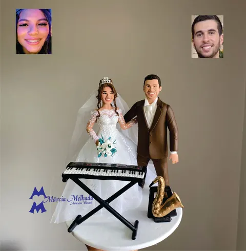 Noivinhos de biscuit com noiva de vestido rendado e noivo de terno marrom, ao lado de um teclado e um saxofone dourado